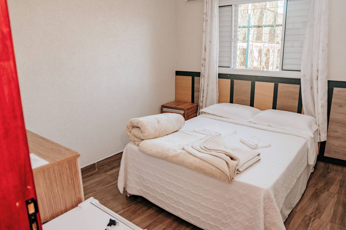A bedroom with a bed, a nightstand, a wooden cabinet, and a window with curtains.