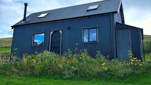 A single-story, dark-colored building with a sloped roof, a chimney, and a small window. - Barn Sleeps 4 With Enclosed Garden (Mold)