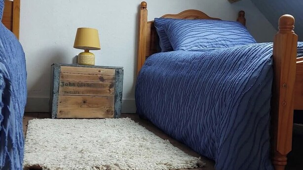 A bedroom with a sloped ceiling, wooden flooring, a bed with blue bedding, a nightstand with a lamp, and a small wooden chest. - Barn Sleeps 4 With Enclosed Garden (Mold)