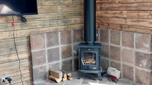 A wood-burning stove in a corner with a stone bench, a TV mounted on the wall, and a power outlet. - Barn Sleeps 4 With Enclosed Garden (Mold)