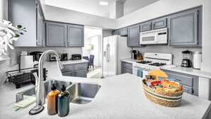 Une cuisine moderne avec des meubles gris, des appareils en acier inoxydable et un îlot central sur lequel se trouve un panier rempli de collations.