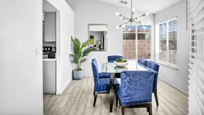 Un coin repas avec une table en verre, des chaises à revêtement bleu, une plante en pot et un lustre moderne.