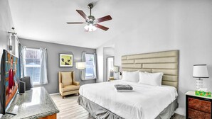 Une chambre d’hôtel équipée d’un lit, d’une chaise, d’un bureau, d’une télévision, d’un ventilateur de plafond et d’une fenêtre avec des rideaux.