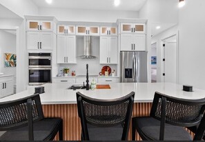 A modern kitchen with white cabinetry, stainless steel appliances, a central island with chairs, and a wooden accent wall.