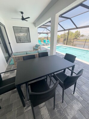 A covered patio area with a pool, outdoor furniture, and a ceiling fan. - Newly Built Modern Vacation Home 4 BR/3 BA Your Own Heated Pool, Lanai on Canal (Cape Coral)