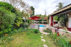 A garden with a pool, red umbrellas, and outdoor seating. - Guest Room “Mitsouko” with Shared Pool, Wi-Fi, and Air Conditioning (Antibes)