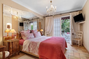 A bedroom with a large bed, a chandelier, a television, and a view of the outdoors. - Guest Room “Mitsouko” with Shared Pool, Wi-Fi, and Air Conditioning (Antibes)