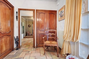 A hallway with wooden doors, a chair, a statue, and a window with curtains.