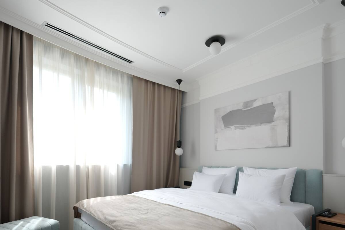 Una habitación de hotel moderna con una cama grande, una mesita de noche, una obra de arte en la pared y una ventana con cortinas.