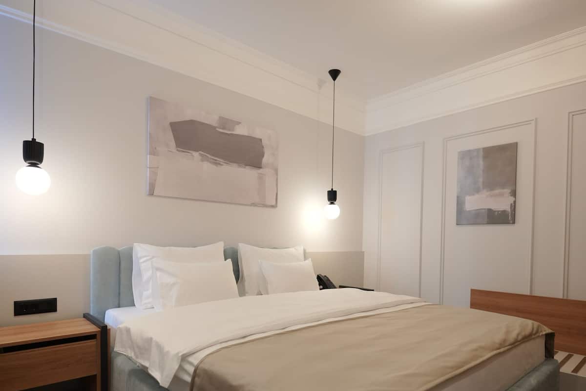 Un dormitorio ordenado con cama, mesitas de noche y una obra de arte colgada en la pared.
