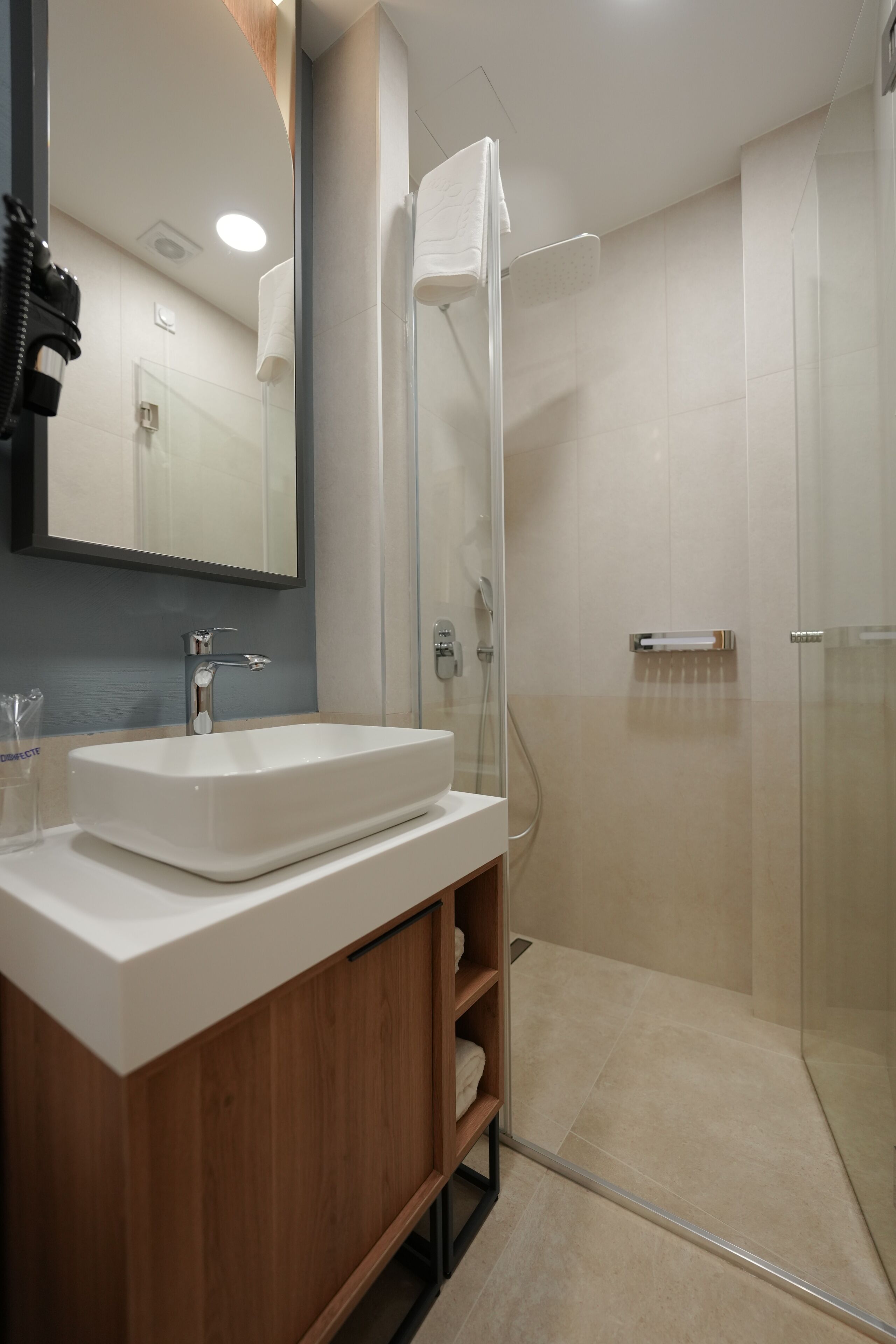 A modern bathroom with a white sink, mirror, and glass shower enclosure.