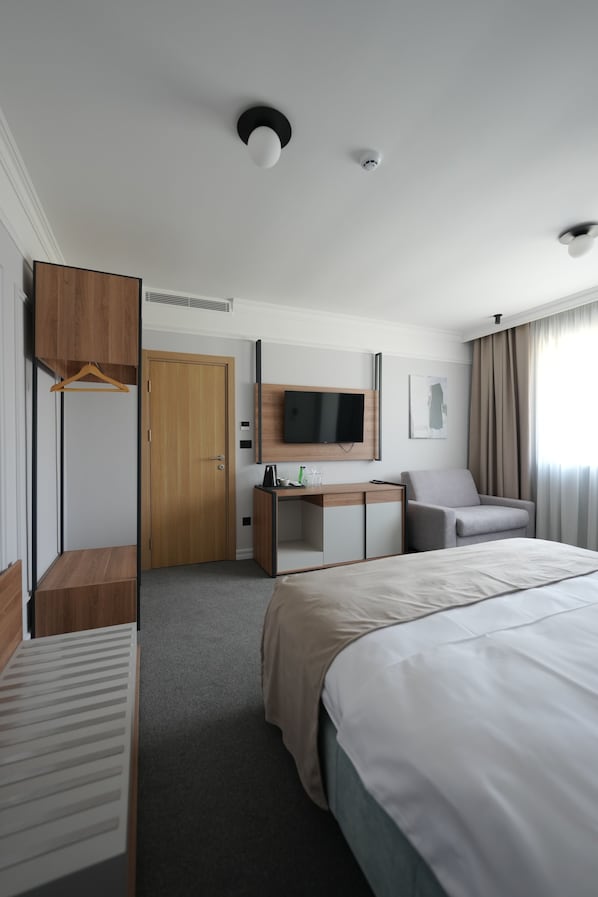 A hotel room with a bed, a desk, a chair, a TV, and a door.