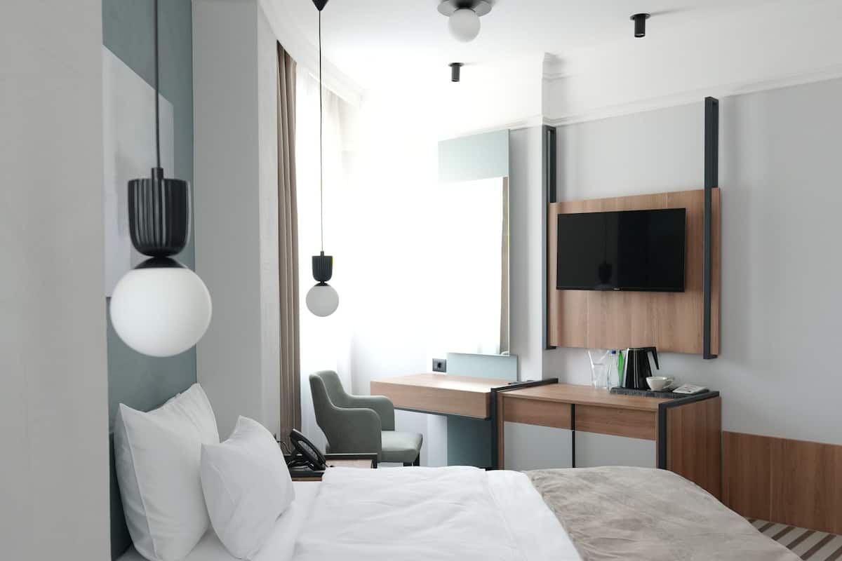Una habitación de hotel moderna con una cama, escritorio, silla y televisor fijado en la pared.