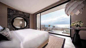 Une chambre avec un grand lit, un miroir rond et une vue sur la mer.