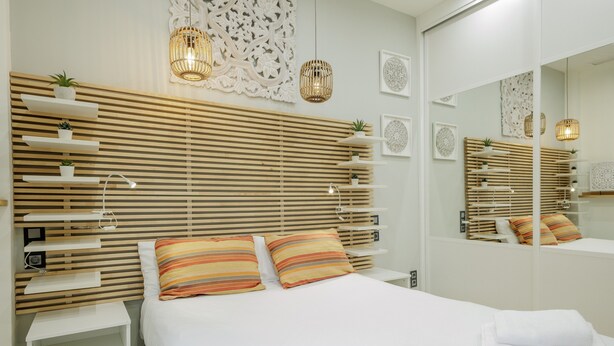 A modern hotel room with a wooden slatted headboard, a large mirror, and a bedside table with a lamp. - Designer Loft at Seville's Alameda — Smart Tech & Wellness Oasis (Sevilla)