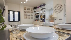 A dining area with white plates, bowls, and cutlery, a woven placemat, and a bookshelf in the background. - Designer Loft at Seville's Alameda — Smart Tech & Wellness Oasis (Sevilla)
