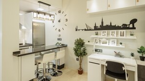 A modern kitchen with a built-in refrigerator, a dining area with bar stools, a desk with a chair, and a wall clock. - Designer Loft at Seville's Alameda — Smart Tech & Wellness Oasis (Sevilla)
