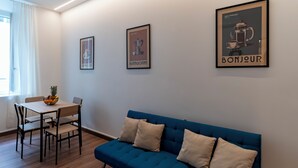 A room with a blue sofa, a dining table with chairs, and three framed posters on the wall. - Venezia Urban Rooms (Livorno)
