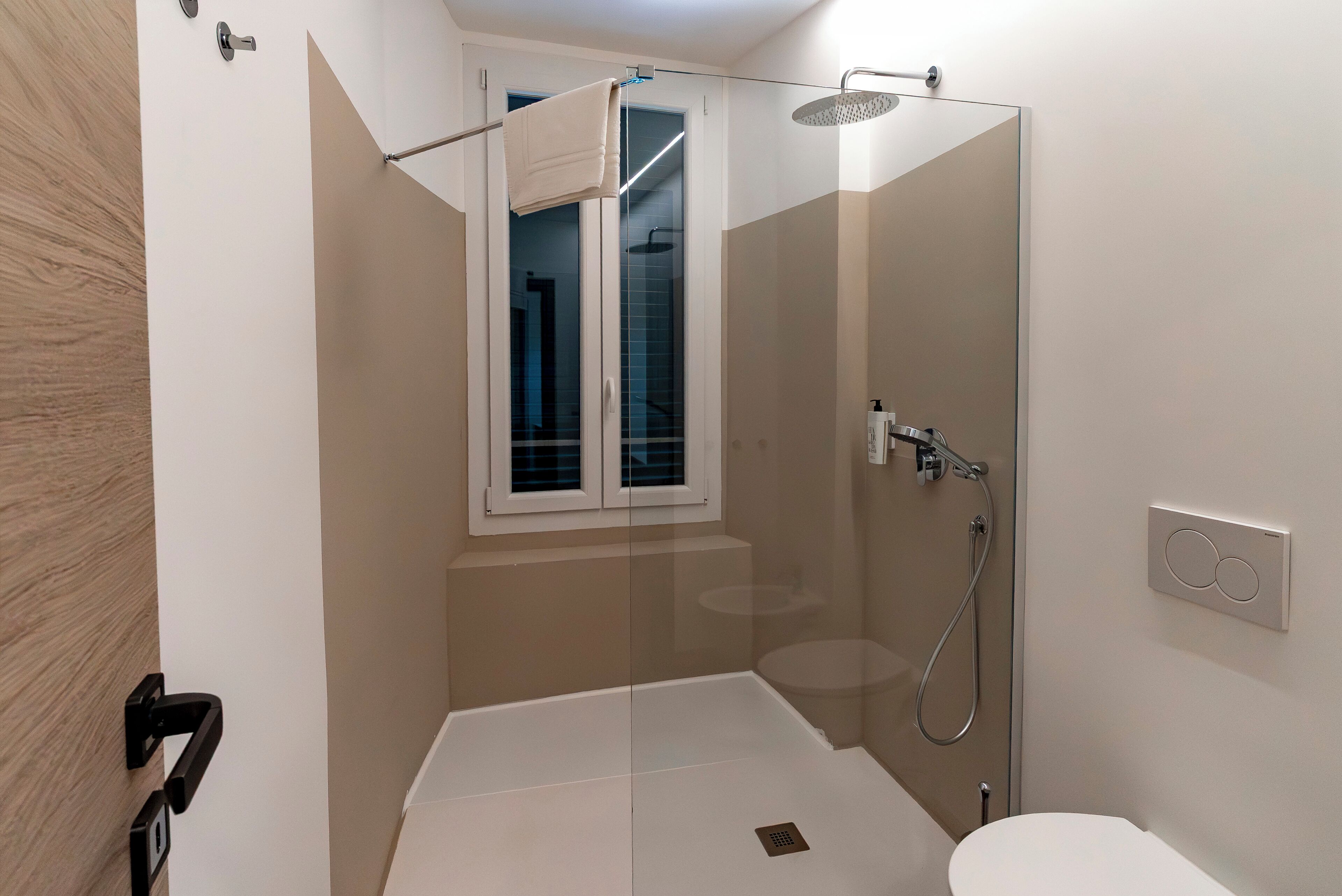 Ein modernes Badezimmer mit einer gläsernen Duschkabine, einer Toilette und einem Fenster.