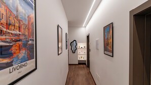 A hallway with framed artwork, a white wall, and a wooden floor. - Venezia Urban Rooms (Livorno)