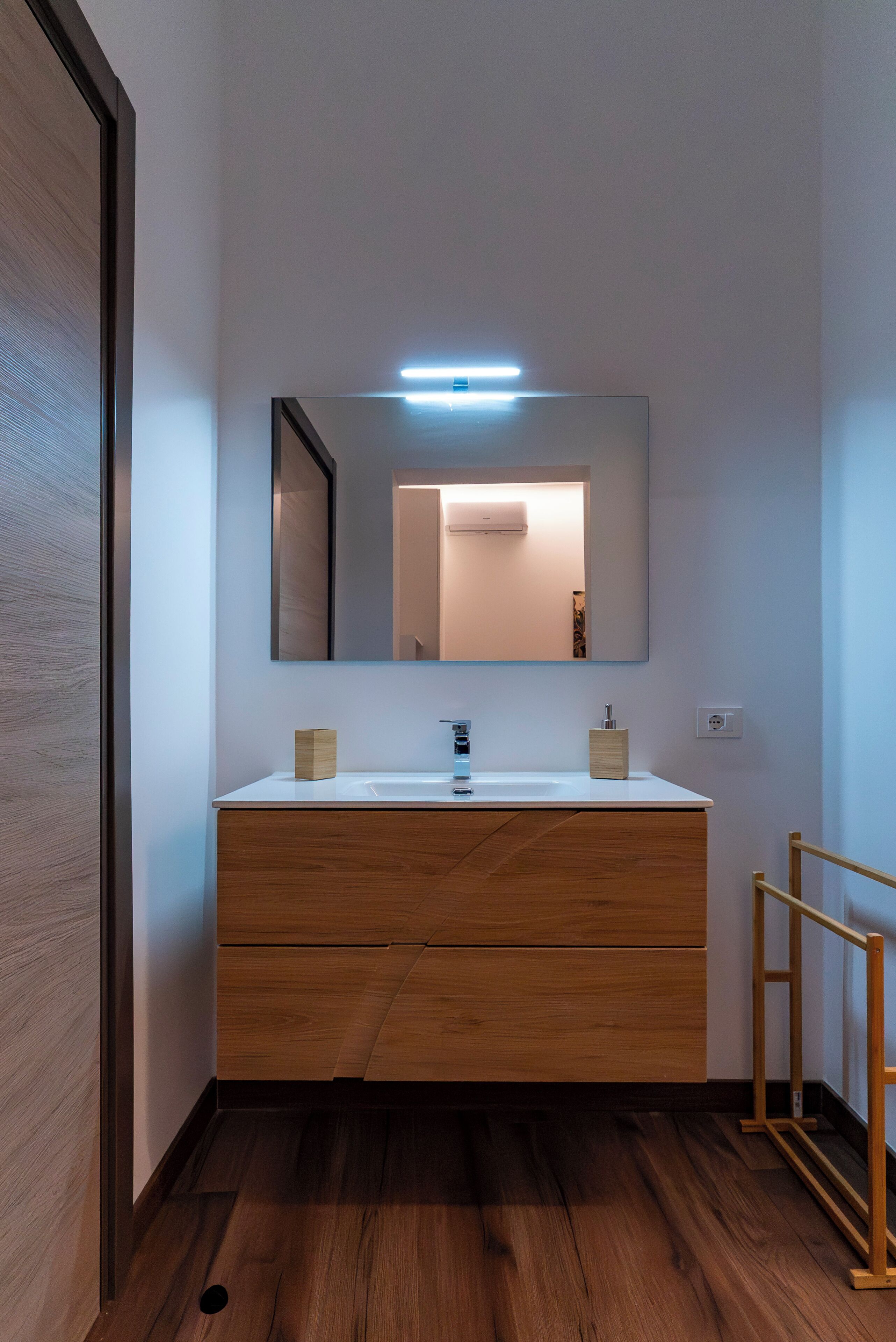 A modern bathroom with a wooden vanity, a large mirror, and a light fixture above the mirror.
