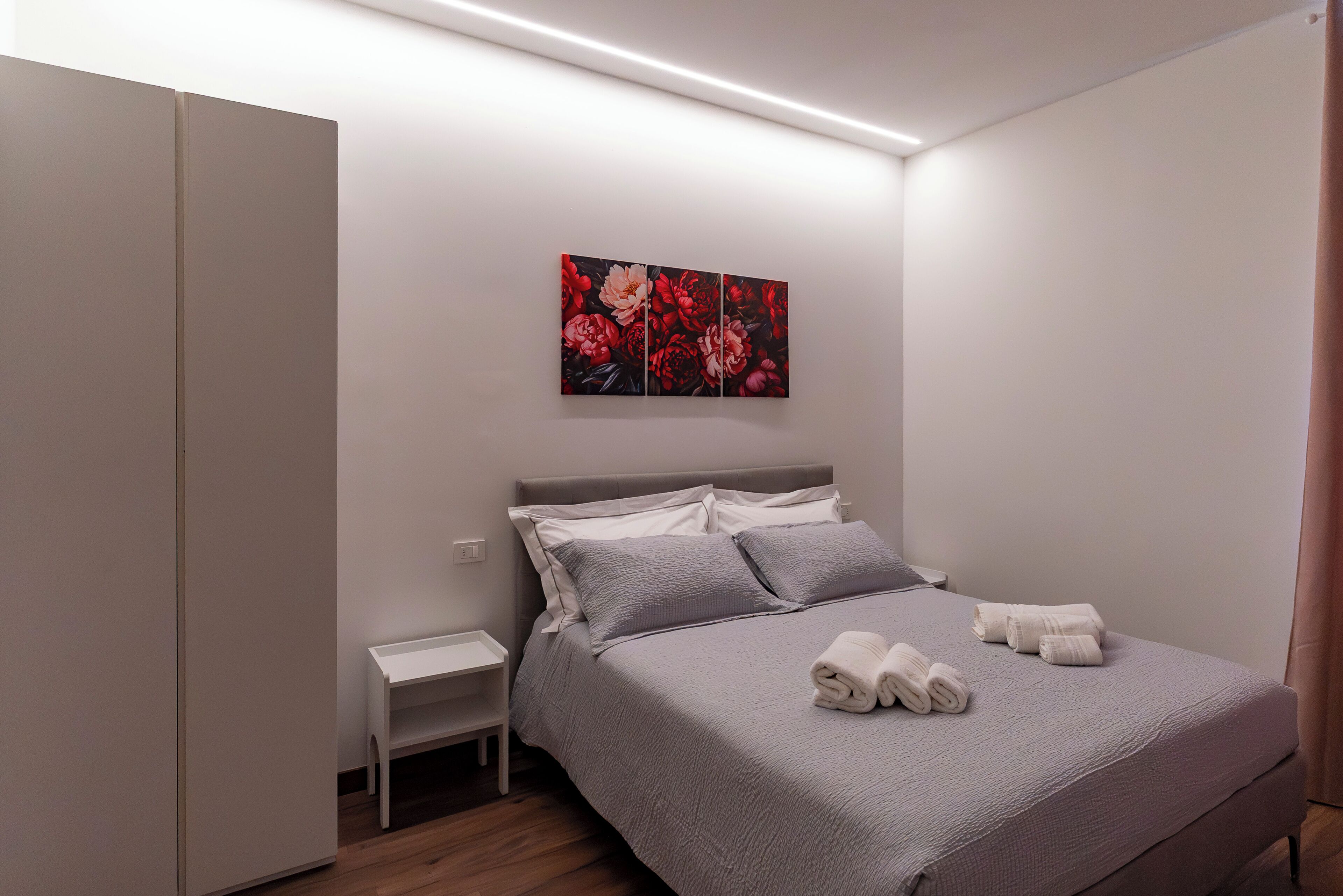 A bedroom with a bed, pillows, a nightstand, a painting, and towels.
