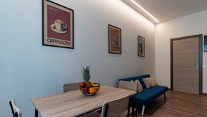 A modern room with a dining table, chairs, a fruit bowl, a sofa, and framed pictures on the wall. - Venezia Urban Rooms (Livorno)