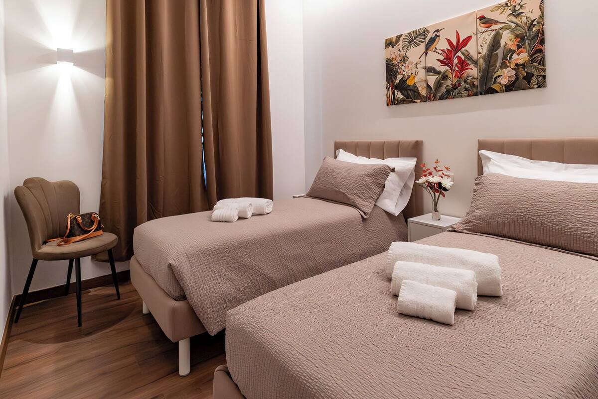 A hotel room with two beds, a chair, a nightstand, and a wall art piece.