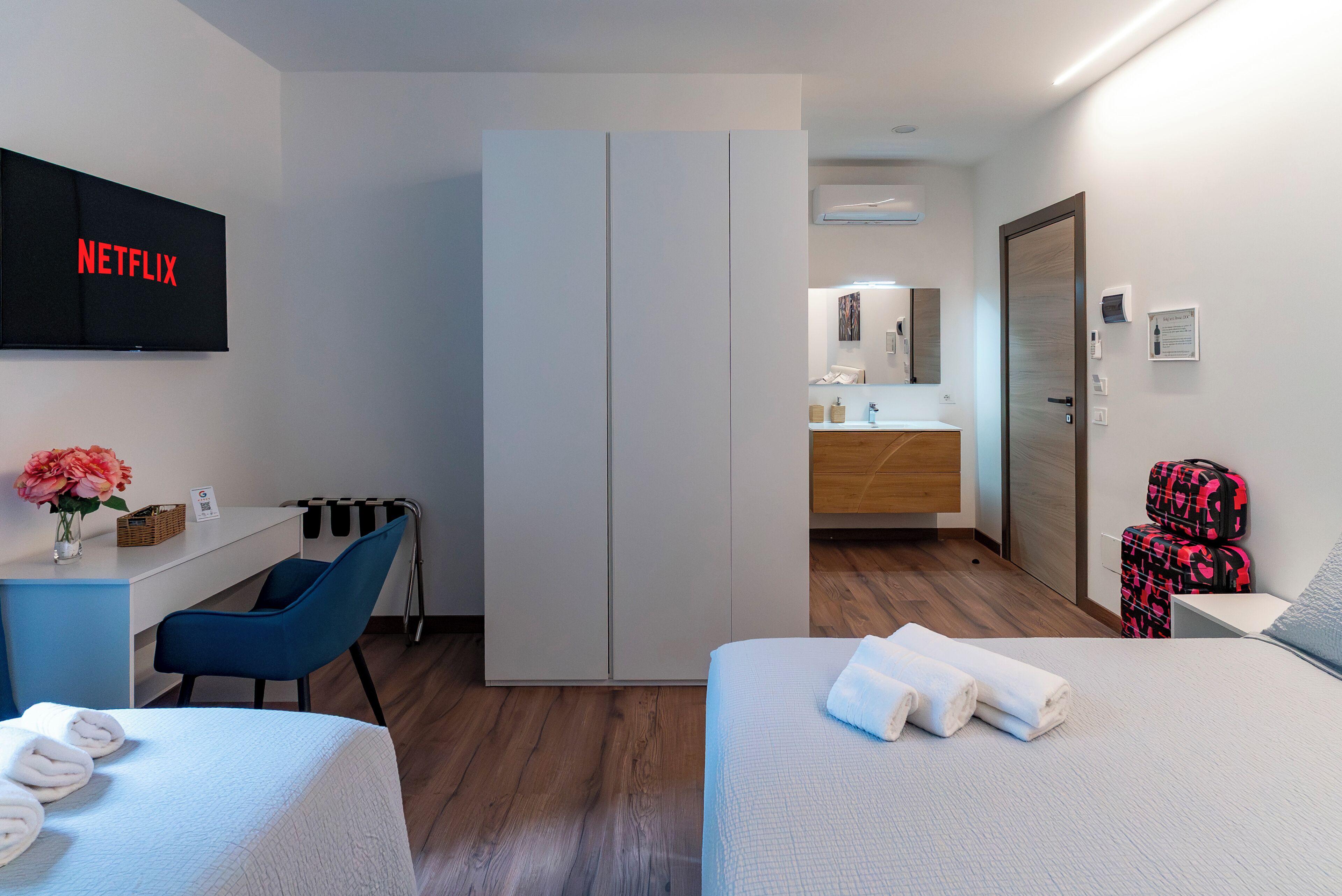 Habitación de hotel con cama, escritorio, silla, armario, televisor, baño y maleta.