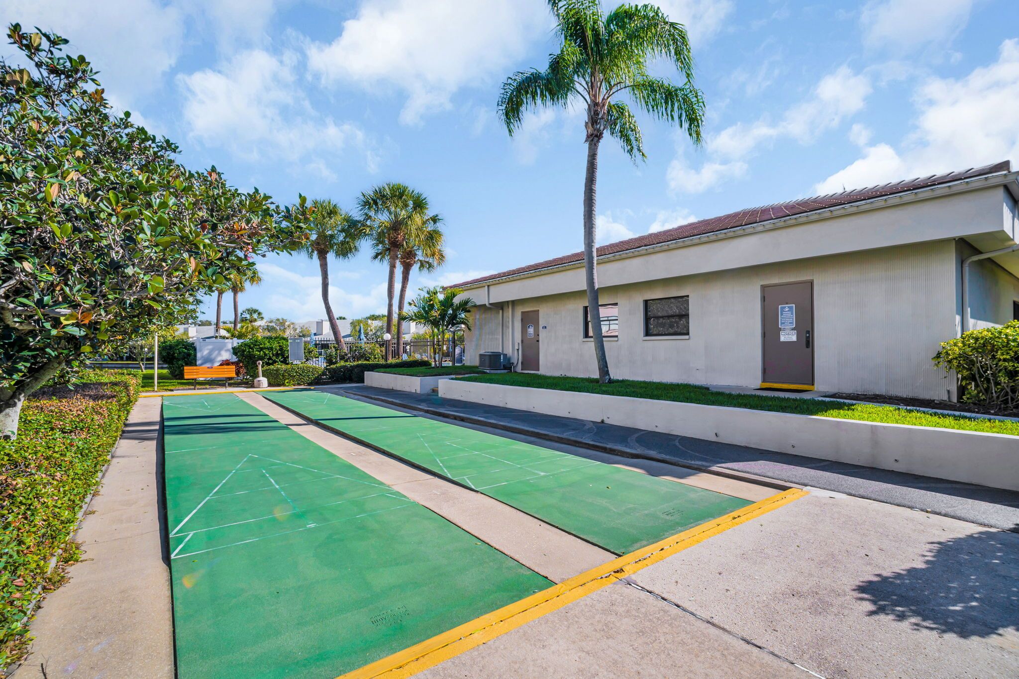 Un patio con canchas de juego de bochas verdes, palmeras y un edificio de techo rojo.