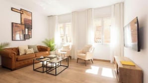 Ein Wohnzimmer mit Sofa, Sessel, Couchtisch und Fernseher an der Wand.