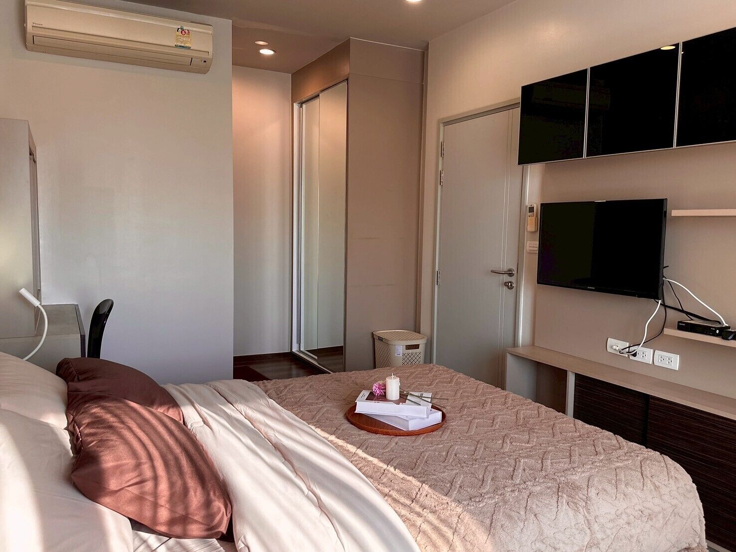 A hotel room with a bed, a television mounted on the wall, a door, and a small table with a basket.
