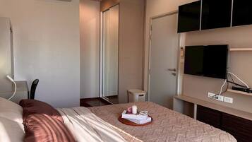 A hotel room with a bed, a television mounted on the wall, a door, and a small table with a basket.
