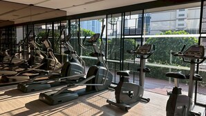 Ett gym med flera motionscyklar och löpband, stora fönster och utsikt över byggnader och grönområden utanför.