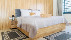 A bedroom with a wooden headboard, a bed with a white bedspread, a nightstand with a lantern, and a window with curtains. - Cozy 1-bedroom apartment in serene Calavi with AC (calavi)