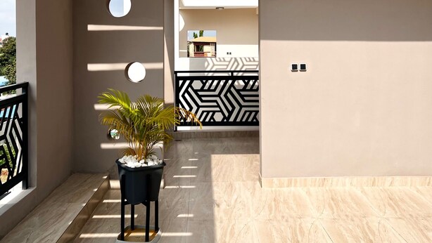 A modern building with geometric wall designs, a potted plant, and a view of another building in the background. - Cozy 1-bedroom apartment in serene Calavi with AC (calavi)