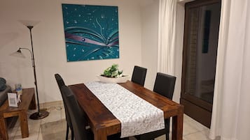 A dining area with a wooden table, black chairs, a decorative wall piece, a floor lamp, and a view through a window.