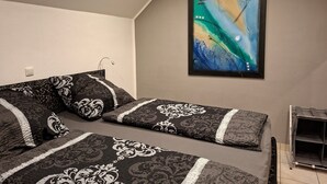 A bedroom with a bed, a wall-mounted abstract painting, and a small shelf unit.