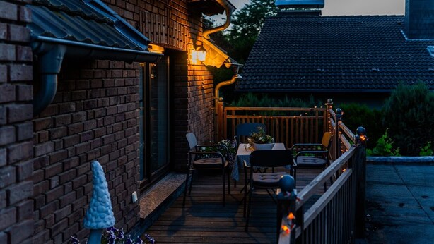 A brick building with a wooden deck, outdoor seating, and a railing.