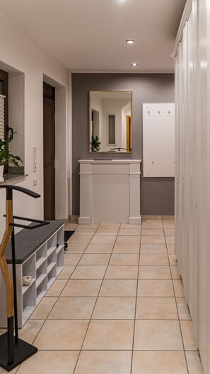 Un couloir avec un sol carrelé, un comptoir blanc avec un miroir et une porte donnant sur une autre pièce.