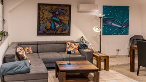 Een woonkamer met een grijze modulaire bank, een houten salontafel, een vloerlamp en twee kunstwerken aan de muur.