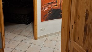 A room with a wooden door, a tiled floor, and a painting on the wall.