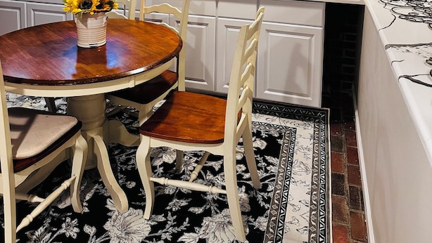 A modern kitchen with white cabinetry, a wooden dining table with chairs, a brick backsplash, and a black and white floral rug. - Cozy room in delightful Wilmington home, close to all local attractions (Wilmington)