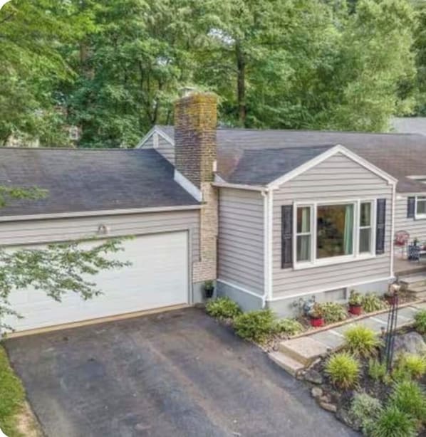 A single-story house with a garage, a chimney, and a small front yard with potted plants.