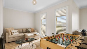 A living room with a sofa, a foosball table, and a window with blinds. - Fair Haven in Cape Woolamai (Cape Woolamai)
