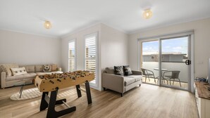 A living room with a foosball table, two sofas, a dining area, and a sliding glass door leading to a balcony. - Fair Haven in Cape Woolamai (Cape Woolamai)