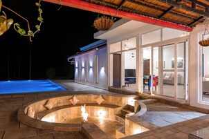 Un patio moderno al aire libre con una chimenea, una piscina y un espacio habitable con paredes de vidrio.