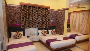 A hotel room with three beds, a wooden headboard, patterned curtains, and a brown rug. - Hotel Royal Inn By Glitz (Mangaluru)