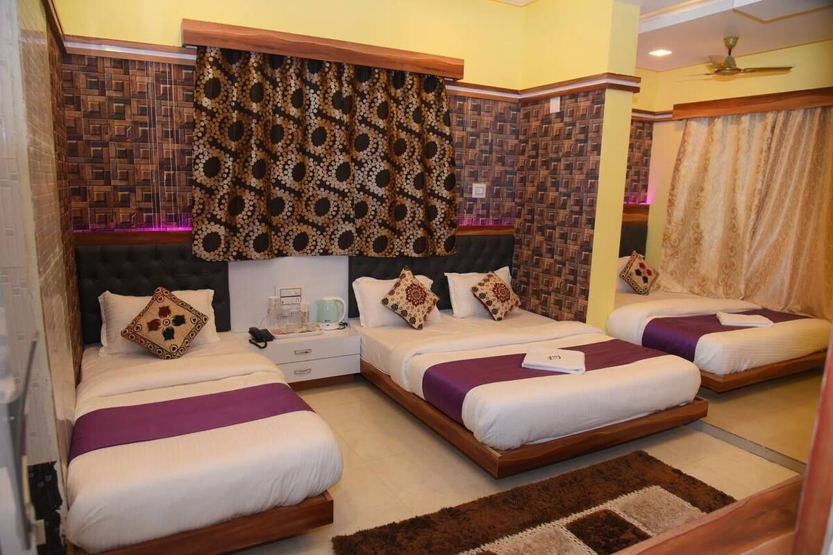 Habitación de hotel con tres camas, cabecera de madera, cortinas estampadas y alfombra marrón.
