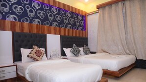 A hotel room with two beds, a wooden headboard, a patterned wall, and a curtain. - Hotel Royal Inn By Glitz (Mangaluru)